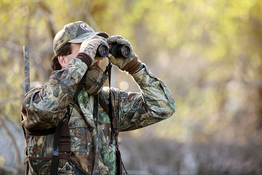 Hunter in a forest wearing camouflage, holding binoculars
