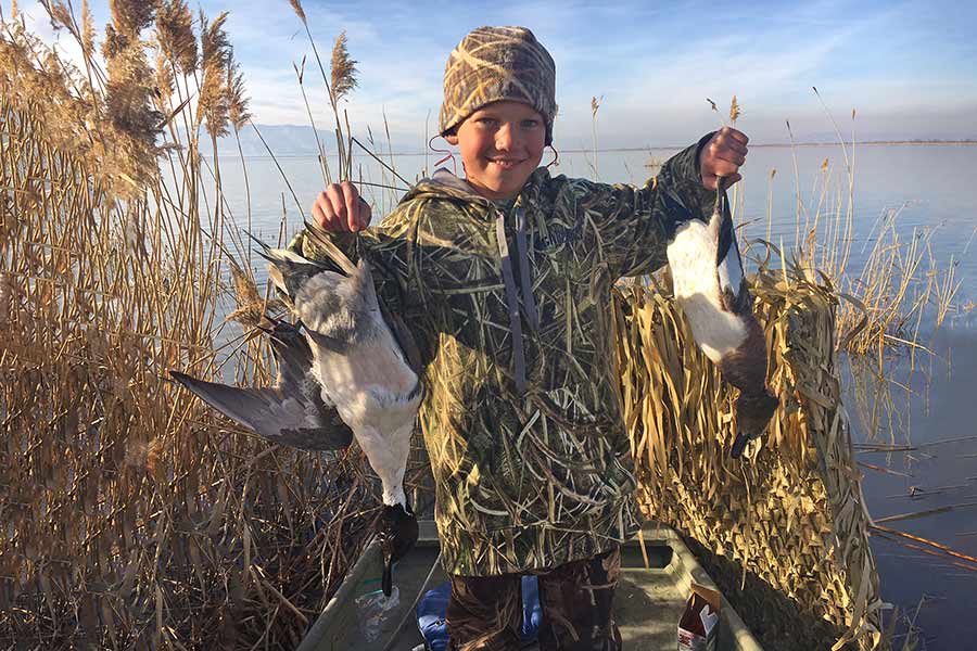 Boy holding harvested ducks at pond