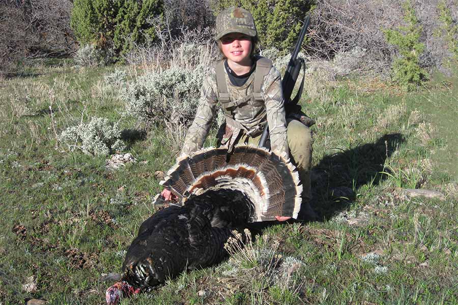 Boy with rifle holding harvested wild turkey on the ground