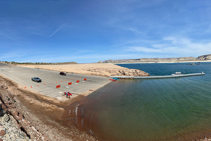 Panoramic view of boat ramp at Lake Powell, with the water level receding and several boaters at the water's edge