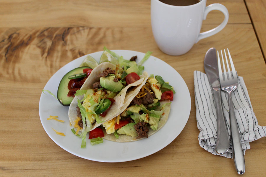 Plate of goose chorizo breakfast tacos, next to a knife and fork and a cup of coffee