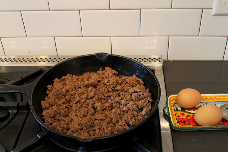 Sausauge being sautéed in a frying pan, next to a plate of two uncracked eggs