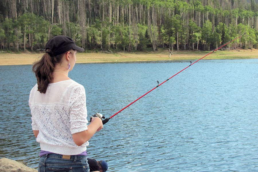 Woman holding a fishing pole at a lake, surrounded by a green forest