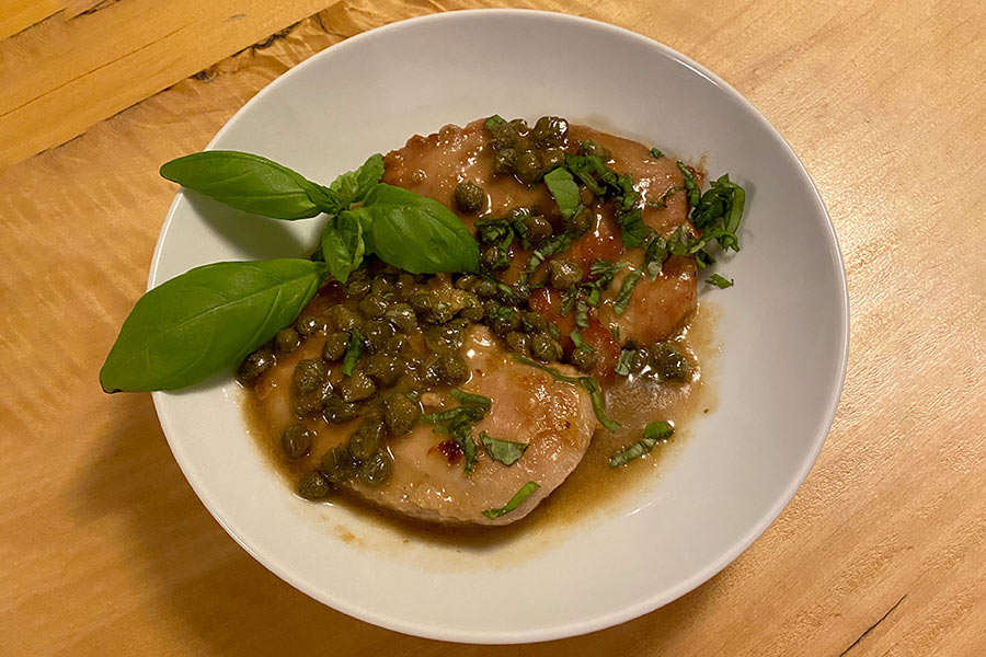 Plate of pheasant piccata, with sauce and capers poured on top and garnished with fresh herbs
