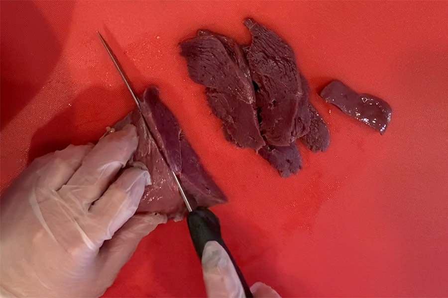 Hands with knife slicing uncooked Canada goose meat