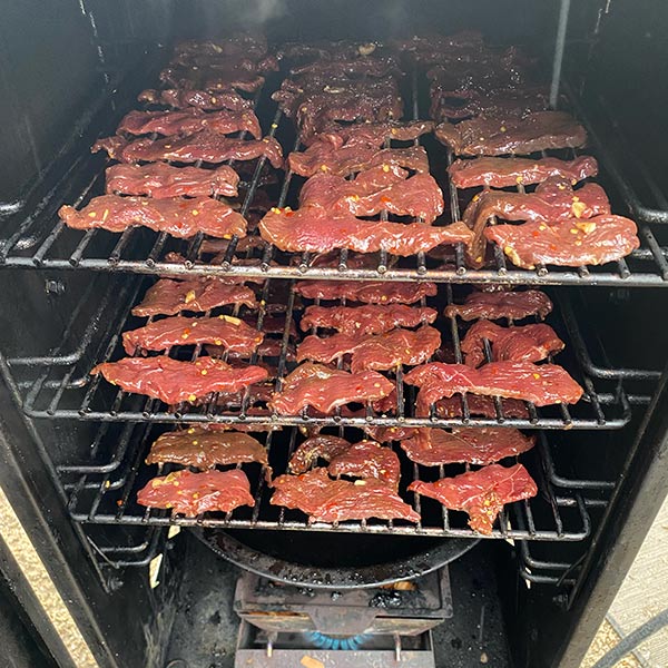 Dozens of strips of goose meat lying on a grill inside a smoker