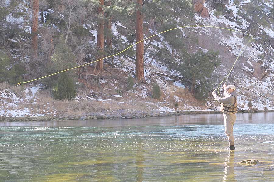 An angler fly fishing in the Green River, with snow on the ground