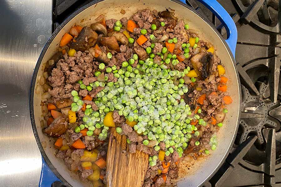Peas, ground elk meat, and mushrooms being stirred around in a saucepan