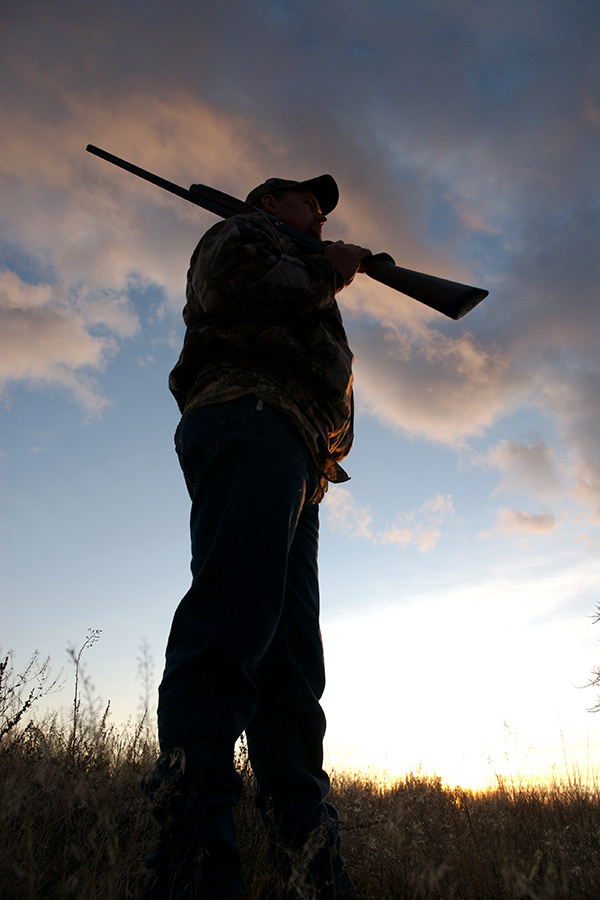 Silhouette of a hunter in a field, carrying a rifle