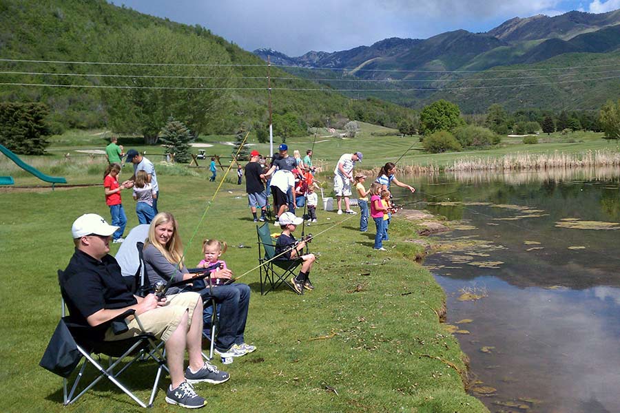 Large group of anglers, including children, fishing at the edge of a pond at Wasatch Mountain State Park