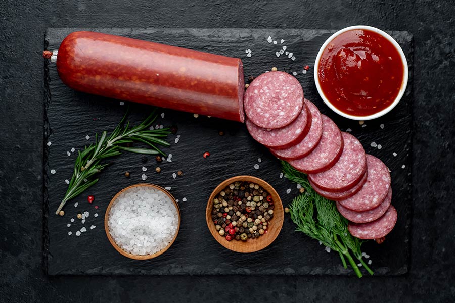 Dry sausage with fresh rosemary and spices on a stone background