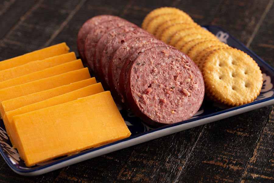 Summer sausage with crackers and cheddar cheese on a rustic wooden table