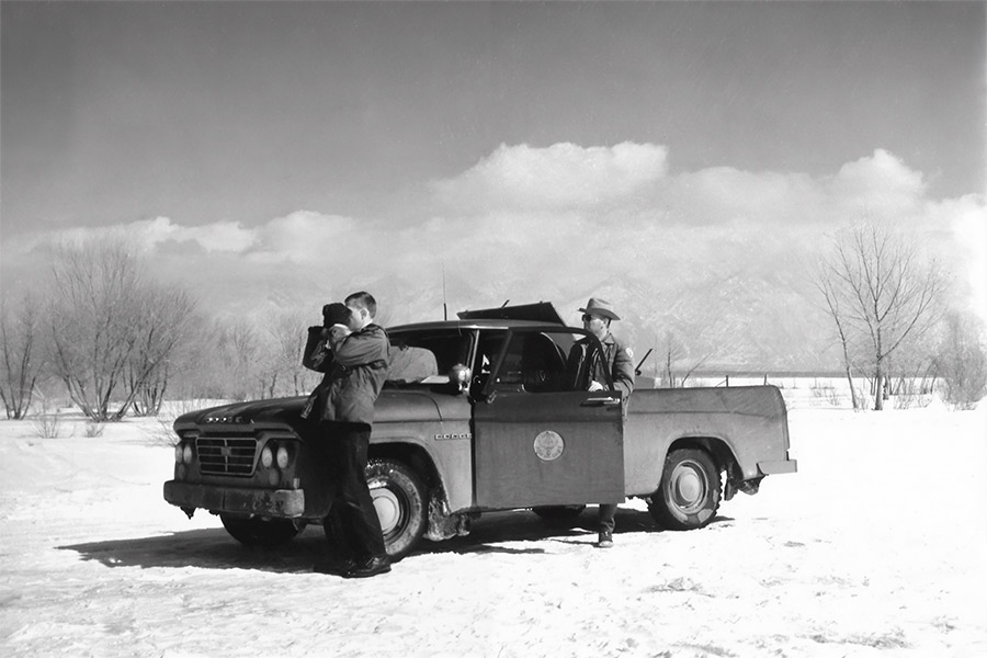 Utah Fish and Game employees, one with binoculars, with a truck in snow at the Ogden Bay Bird Refuge