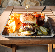Grilled bison slider in a bun on a tray with chips and sauce