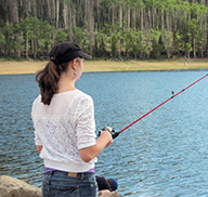 Woman holding a fishing pole at a lake, surrounded by a green forest