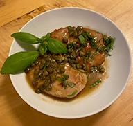 Plate of pheasant piccata, with sauce and capers poured on top and garnished with fresh herbs