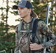 Female hunter with muzzleloader and gear walks in the forest