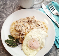 Plate of biscuits and gravy with bits of pronghorn sausage crumbled into the gravy, served with a fried egg over easy