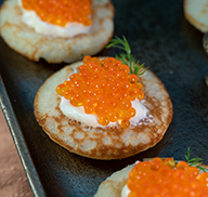 Small pancakes topped with golden whitefish caviar and sour cream