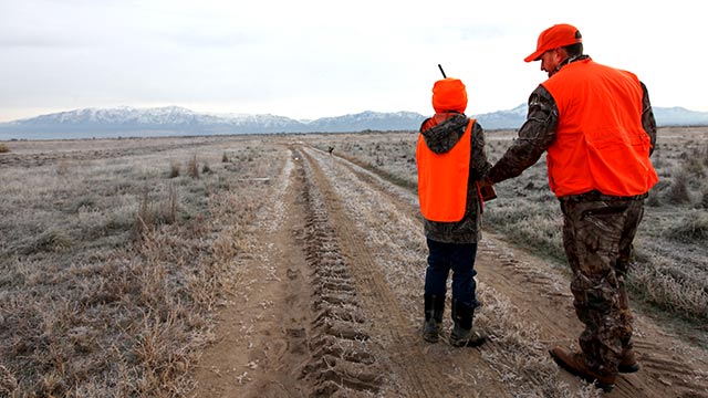 Father and son, dressed in hunter orange, walking along a dirt road in an open field