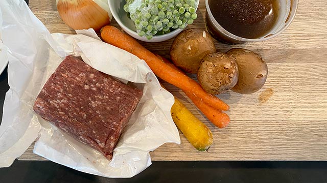 Slab of raw ground elk meat and frozen vegetables on a cutting board