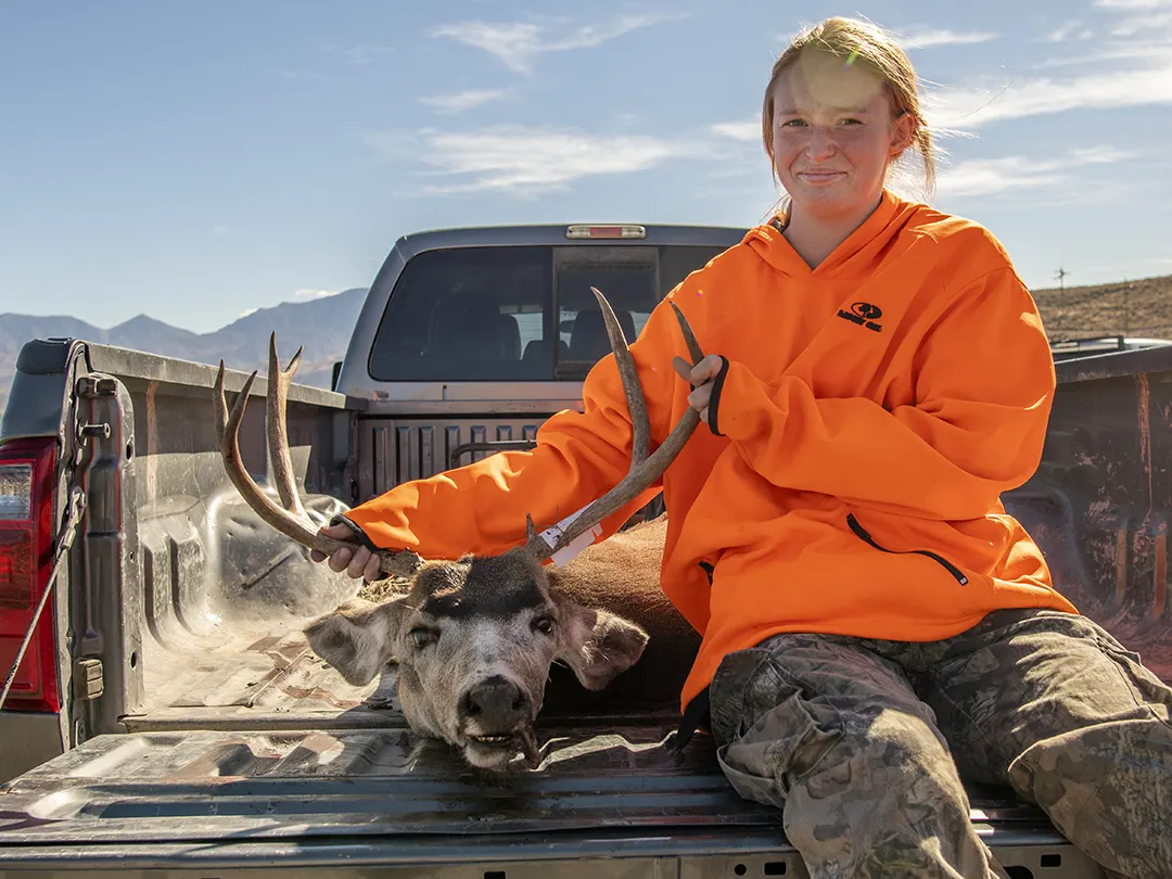 Young hunter sitting in a truck bed with a harvested deer