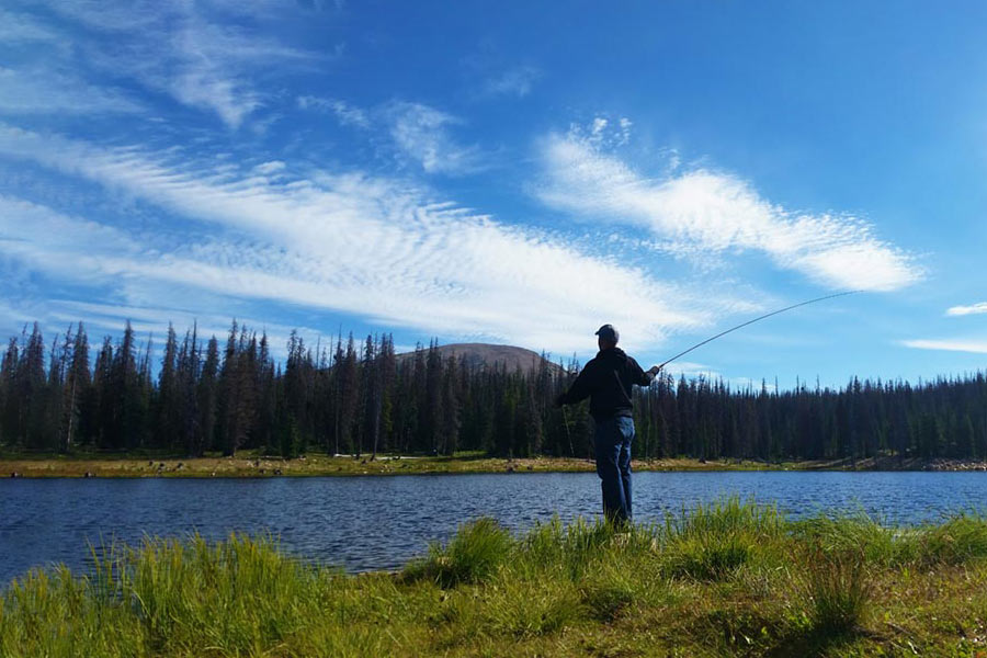 Man standing at a pond in the Unita Mountains, casting in a fishing line