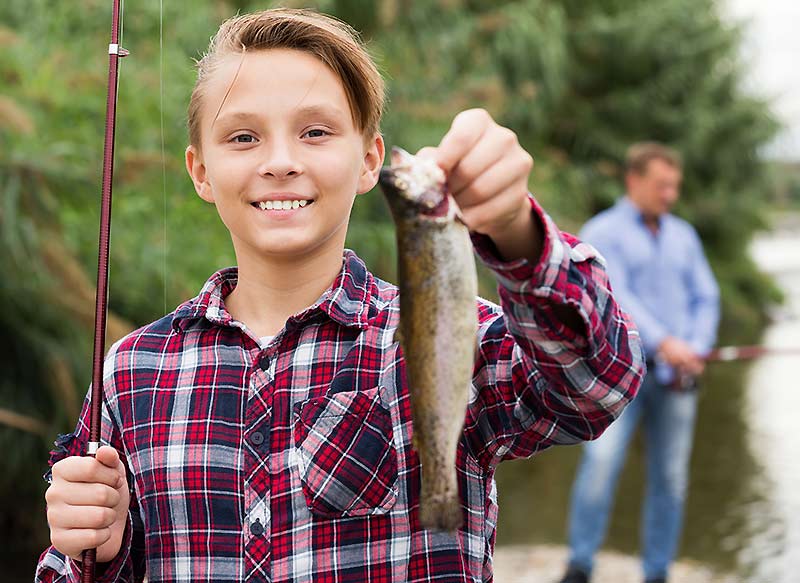 Young boy holding up fishing rod and fish stock photo