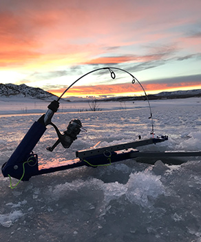 Fishing pole set up in a hole in a drilled hole in the ice, at sunset
