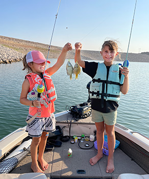 Two young girls, each holding a small, caught panfish in a fishing boat
