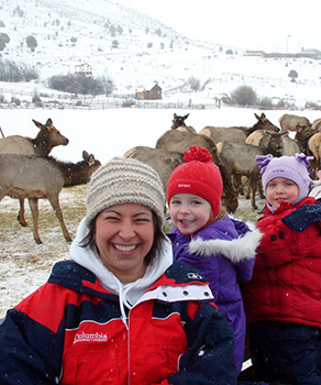 An adult and children sitting in a wagon, riding through a meadow with wild elk at Hardware WMA