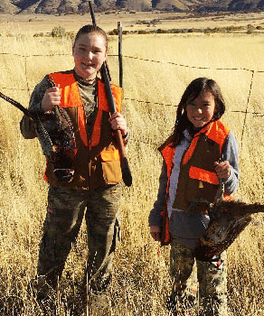 Two youth hunters wearing hunter orange, each holding a harvested pheasant