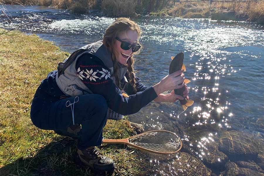 Sarah Wiser holding a caught fish near a shimmering river