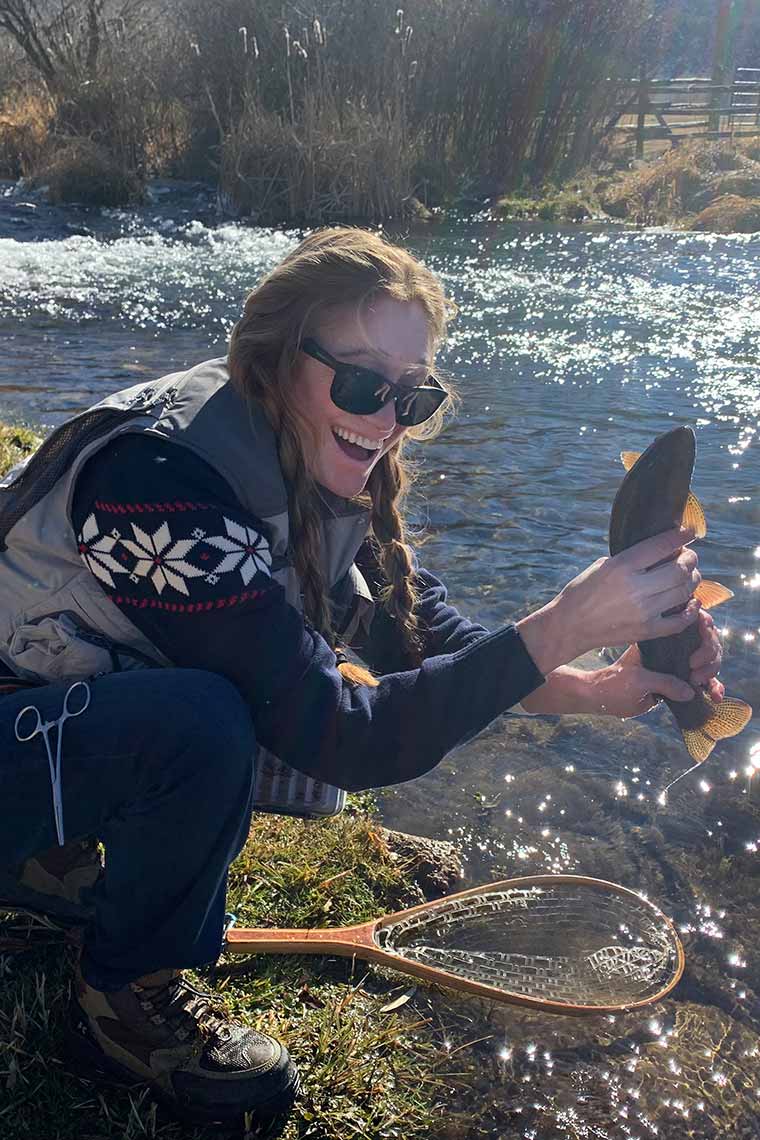 Sarah Wiser holding a caught fish near a shimmering river