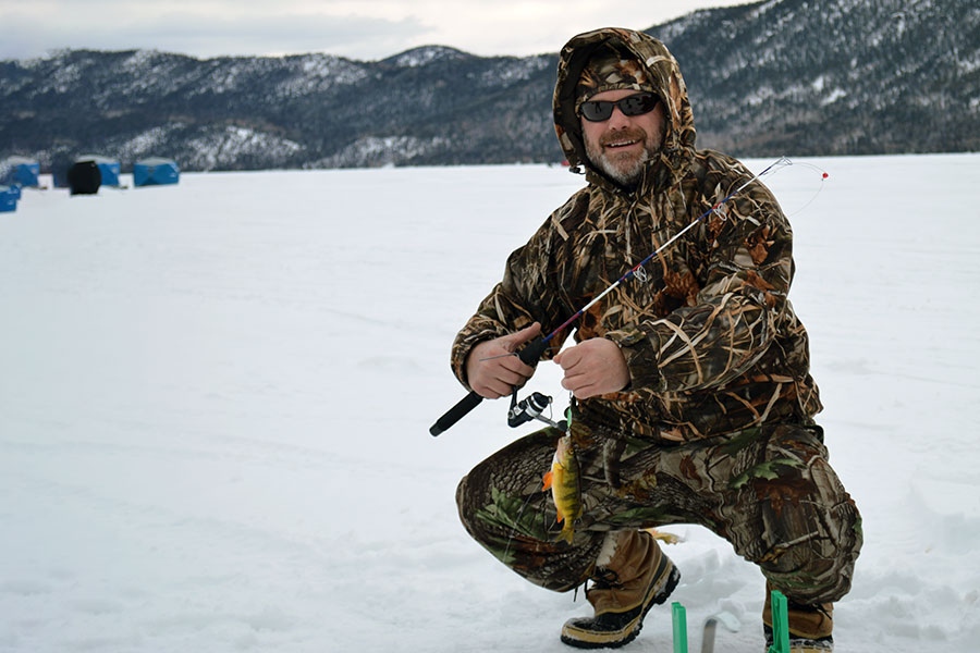 Angler sqatting on ice and snow, holding a perch