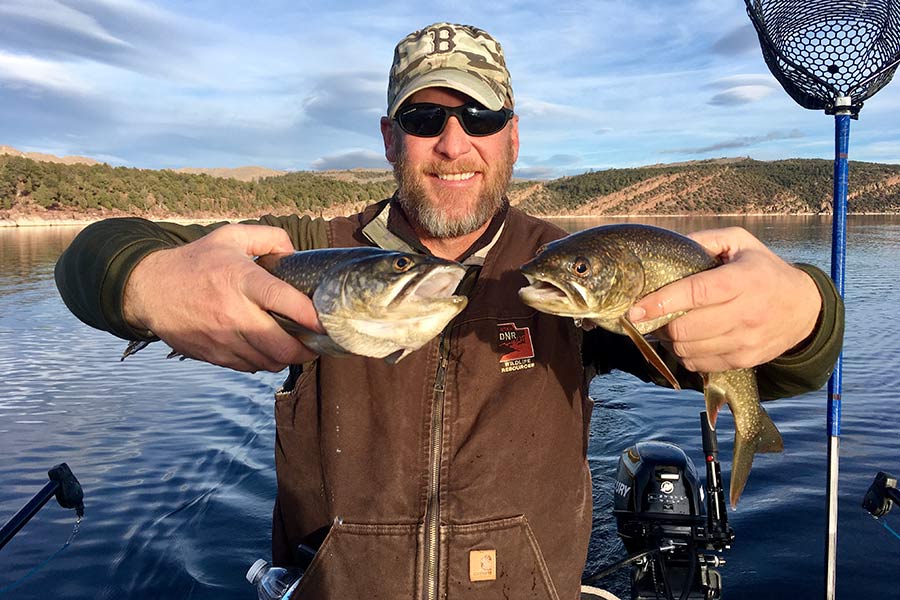 Division of Wildlife Resources employee holding two caught trout in a boat at Flaming Gorge
