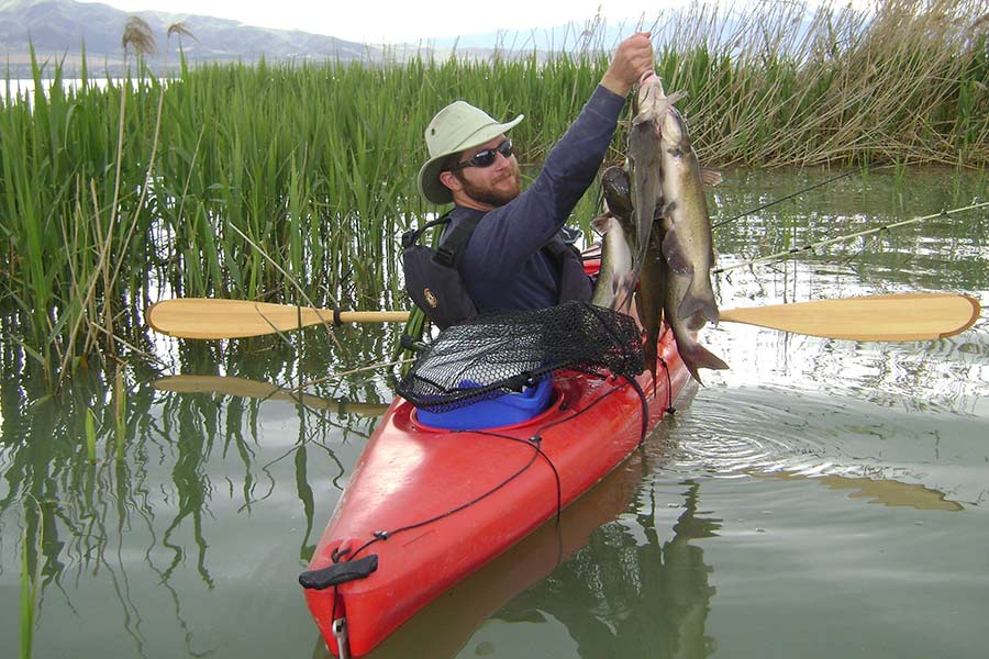 Angler in a kayak holding a group of channel catfish caught at Utah Lake