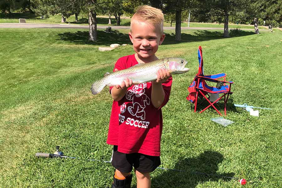 Boy standing in grass, holding a caught rainbow trout