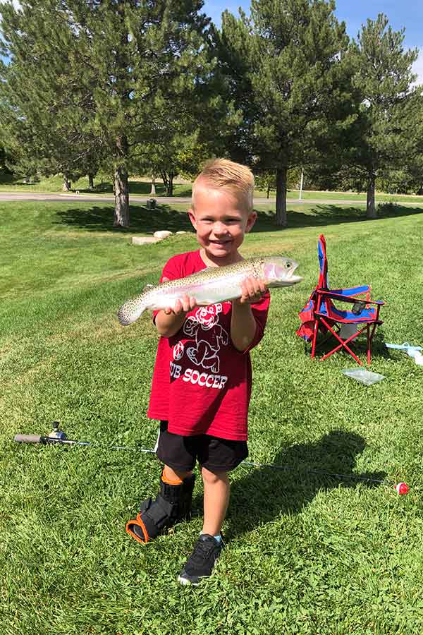 Boy standing in grass, holding a caught rainbow trout