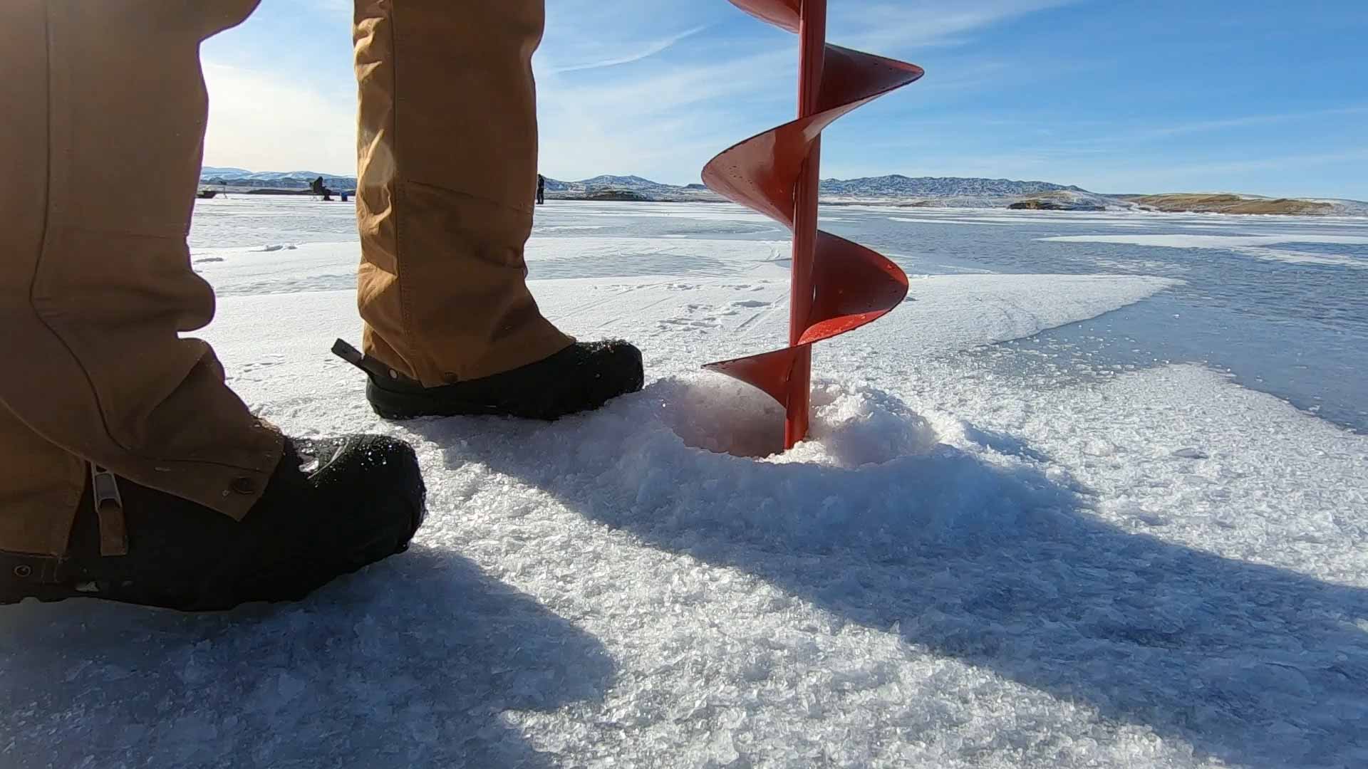 Red auger drill boring through ice on a frozen lake