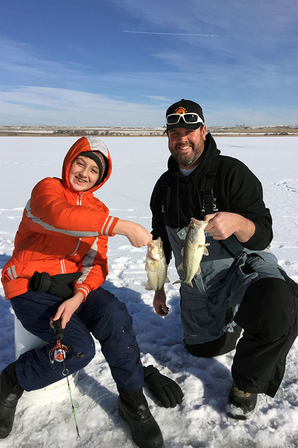 Father and son holding largemouth bass while ice fishing over a frozen lake