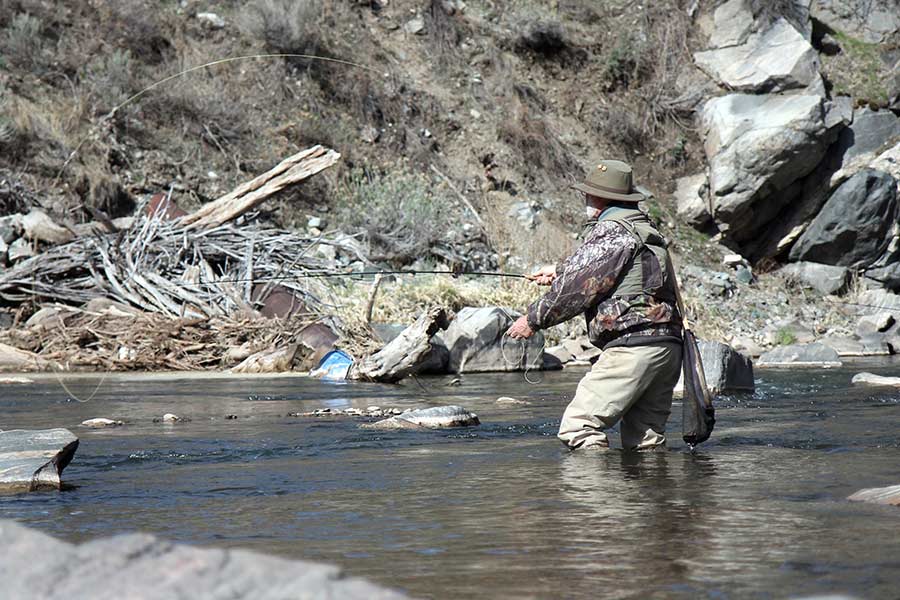Male fly angler, from behind, casting a fishing line into the Weber River
