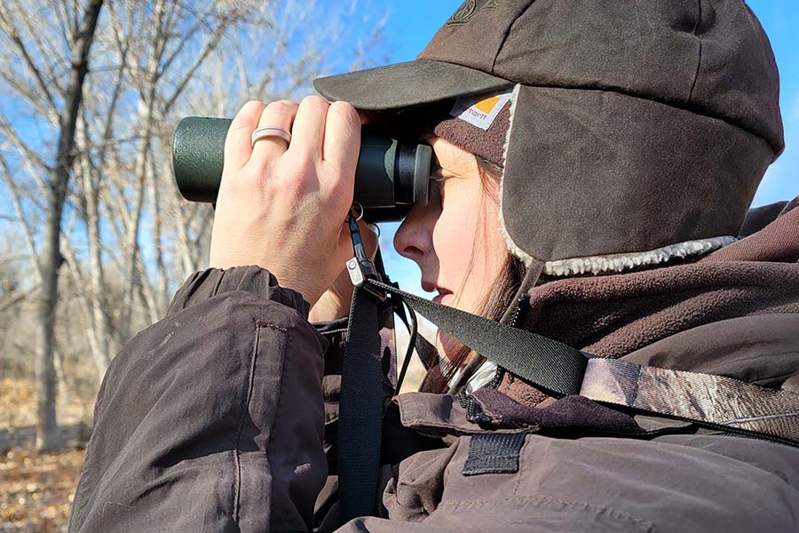 Woman in winter clothing watching birds through binoculars