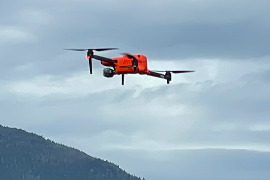 Drone hovering in the air above a field with mountains in the background